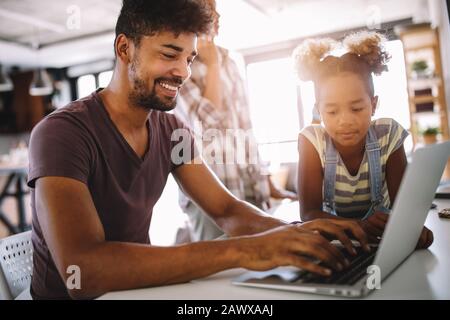 Vater und Tochter arbeiten am Laptop. Geschäftsmann, der von zu Hause aus arbeitet und das Kind beobachtet Stockfoto