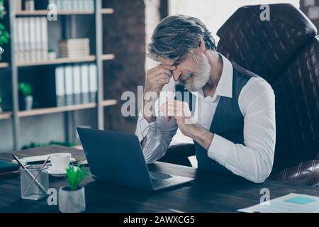 Nahporträt seines hübschen hübschen hübschen hübschen, müden grauhaarigen Mannes, der im Stuhl sitzt und an einem Arbeitsplatz im industriellen Loft-Stil unter Schmerzen leidet Stockfoto