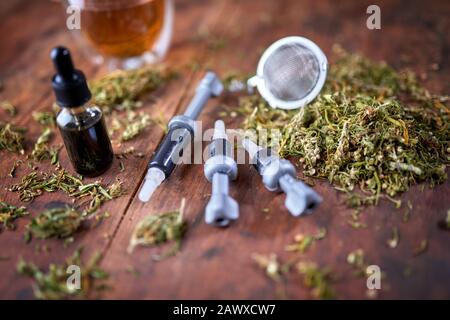Medizinisches Marihuana-Konzept - CBD-Öl, CBD-Paste, getrocknete Marihuana-Blätter. Injektion von CBD-Öl, CBD-Paste, getrockneten Marihuana-Blättern auf Holzhintergrund. Stockfoto