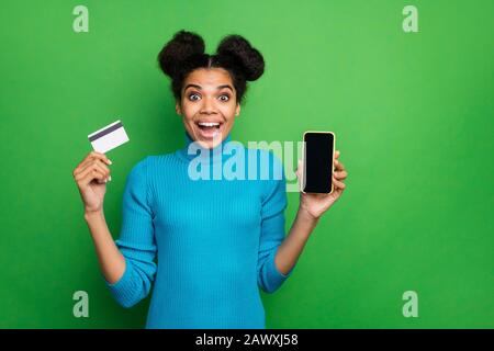 Foto der lustigen dunklen Haut-Dame Telefon Smartphone Smartphone neues Modell Preisberatung verwenden Kreditkarte schnelle Zahlung tragen blauer Pullover isoliert grün