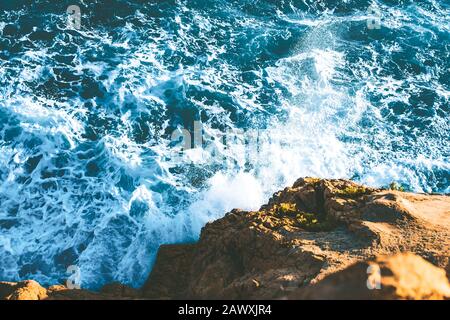 Blick auf die Meereswellen, die am Strand auf Felsen treffen, mit türkisblauem Meerwasser. Felsklippe an der Küste des Atlantiks. Wasser in Co. Spritzt Stockfoto