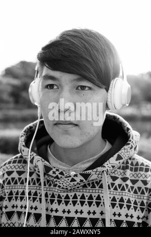 Junger asiatischer Teenager, der Kopfhörer trägt, während er sich im Park entspannen kann Stockfoto