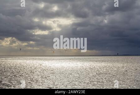 Dramatische beleuchtete Küstenlandschaft, darunter einige Kitesurfer bei Neuharlingersiel in Ostfriesland Stockfoto