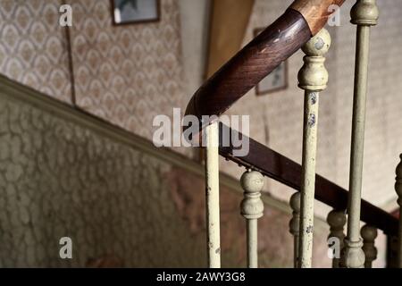 Nahholzwand mit Eisenbalustern auf einer Treppe eines alten und baufälligen Hauses. Gemusterte Vintage-Tapete an der Wand. Stockfoto