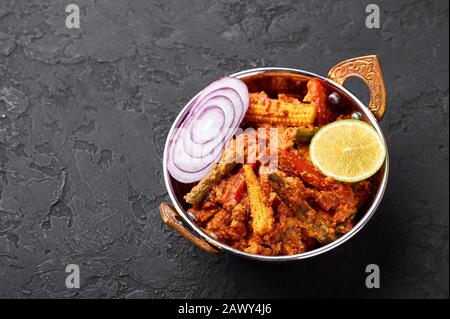 Gemüsejalfrezi in Kupferkadai auf schwarzem Schieferhintergrund. Jalfrezi ist ein Gericht der indischen Küche mit gebratenem Gemüse und Tomaten-Nüssen-Soße mit sp Stockfoto