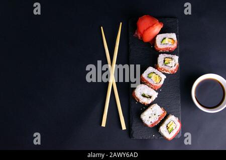 Rollen auf einem Granitständer für Sushi sind in Form eines Drachens ausgelegt, neben Stangen für Sushi und Sojasoße. Stockfoto