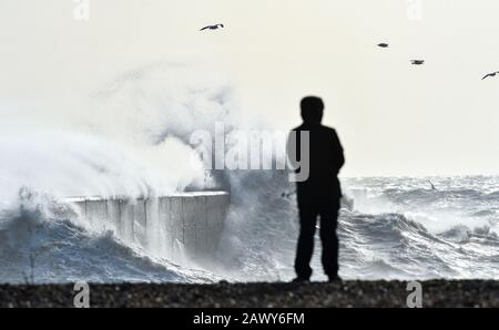 Shoreham UK, 10. Februar 2020 - EIN Wanderer beobachtet, wie die Wellen am Eingang des Shoreham Harbour in Sussex einbrechen, während das Schlussende von Storm Ciara nach und nach durch Großbritannien bläst, nachdem er am Wochenende den Großteil des Landes gebeutelt hatte: Credit Simon Dack/Alamy Live News Stockfoto