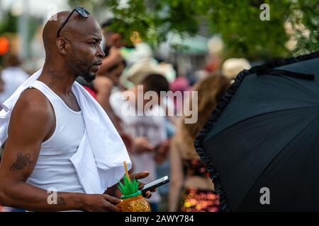 Brooklyn, New York City, USA - 22. Juni 2019: Jährliche Mermaid-Parade der Coney Islands, afrikanischer Mann mit Getränkegrug, der in Menschenmenge steht und auf Smartph blickt Stockfoto