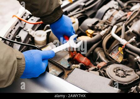 Kfz-Mechaniker, der ein Fahrzeug mit einem Schraubenschlüssel befestigt. Außenhänder des Automechanikers mit einem Schlüssel, der in der Garage arbeitet. Mann mit Handschuhen Stockfoto
