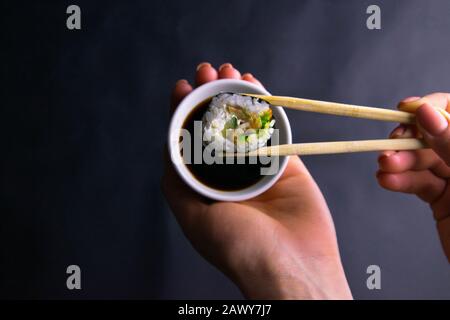 Stöcke rasieren die Rolle von Mohn über einen Teller Sojasoße, eine Platte in einer schönen weiblichen Hand über einem schwarzen Hintergrund Stockfoto