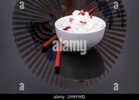Schüssel mit gekochtem weißem Reis, garniert mit essbaren Rosenblättern Stockfoto