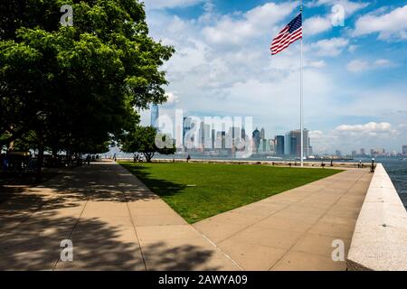 New York, USA - 7. Juni 2019: Amerikanische Flagge auf Ellis Island im New Yorker Hafen und in der Skyline von Manhattan Stockfoto
