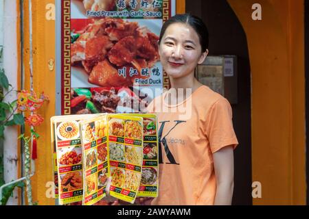 Junge Frau, die als Kellnerin arbeitet und ein Menü aus dem Restaurant zeigt, in dem sie arbeitet, Chinatown, Singapur, Asien Stockfoto