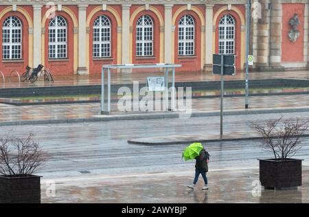 Potsdam, Deutschland. Februar 2020. Eine Frau mit grünem Regenschirm schützt sich vor Regen und Wind vor der Kulisse des Filmmuseum, nachdem der Sturm 'Sabine' Deutschland in der Nacht getroffen hat. Kredit: Soeren Stache / dpa-Zentralbild / ZB / dpa / Alamy Live News Stockfoto