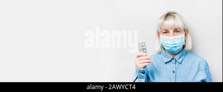 Blonde Erwachsene Frau in einer medizinischen Maske und hält Pillen in den Händen auf einem grauen Hintergrund mit Platz für Text. Kann für Webbanner oder Artikel verwendet werden. SARS Stockfoto