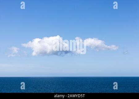 Cumulus-Wolken bilden sich in einem klaren blauen Himmel über einem ruhigen Ozeanhorizont Stockfoto