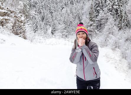 Junge Frau mit farbiger Kleidung bläst im Winter in gefrorenen Händen. Platz für Text Stockfoto