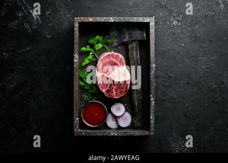 Roher, frischer, quer geschnittener Kalbsschank für die Herstellung von Osso Buco mit Gewürzen und Kräutern auf schwarzem Grund. Draufsicht. Freier Speicherplatz für Ihren Text. Stockfoto