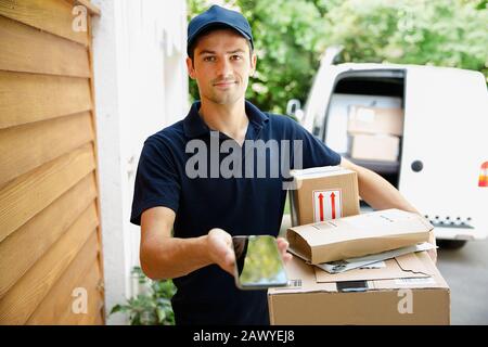 Portrait selbstbewusster Lieferer mit Smartphone vor der Tür Stockfoto