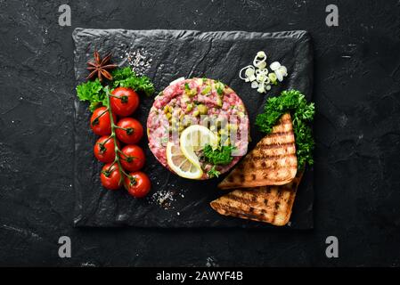 Beef Steak Tatar mit rohem Eigelb, Avocado, Kapern und Zwiebeln. Französische Küche. Draufsicht. Freier Speicherplatz für Ihren Text. Stockfoto