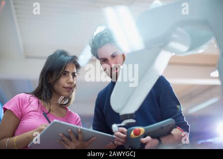 Ingenieure mit digitalem Tablett programmieren Roboterarm im Büro Stockfoto
