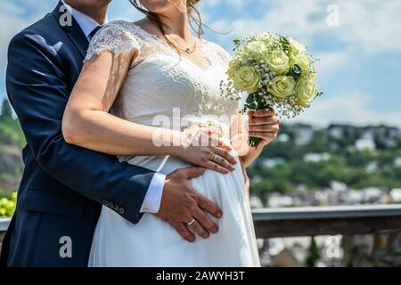 Hände Bräutigam und Brautpaar mit Hochzeitsringen und Blumenstrauß auf dem schwangeren Bauch Baby Liebe Familiensymbol. Stockfoto