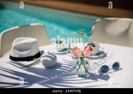 Rosen und Kaffee auf dem sonnigen Terrassentisch am Pool Stockfoto