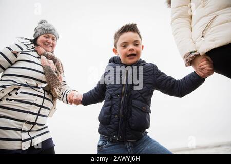 Portrait glücklicher unbeschwerter Junge mit Daunen-Syndrom, das die Hände mit der Mutter hält Stockfoto