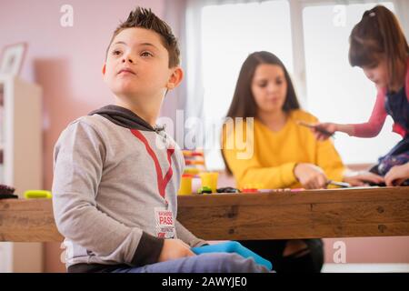 Neugieriger Junge mit Down-Syndrom, der am Tisch spielt Stockfoto