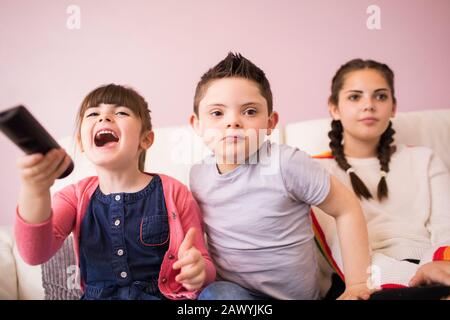 Schwestern und Bruder mit Down-Syndrom Fernsehen auf dem Sofa Stockfoto