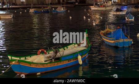 Bunte Boote auf dem ruhigen Wasser der mediterranen Meeresbucht in Malta bei dunkler Nacht mit künstlichem Licht Stockfoto