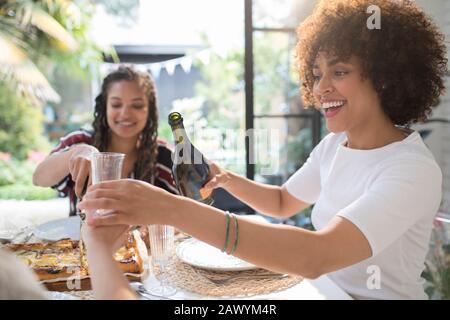 Fröhliche junge Frau, die Wein für einen Freund am Tisch gießt Stockfoto