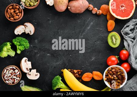 Die Nahrung enthält natürliches Kalium. K: Kartoffeln, Pilze, Banane, Tomaten, Nüsse, Bohnen, Brokkoli, Avocados. Draufsicht. Auf schwarzem Hintergrund. Stockfoto