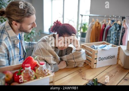 Verunglücktes junges Mädchen in Plaid, neben Wohltätigkeits-Essenskisten. Stockfoto