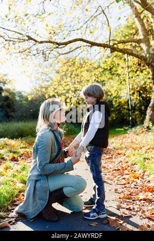 Mutter und Sohn halten Hände und reden im sonnigen Herbstpark Stockfoto