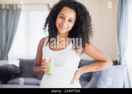 Portrait fröhliche junge schwangere Frau trinkt gesunden grünen Smoothie Stockfoto