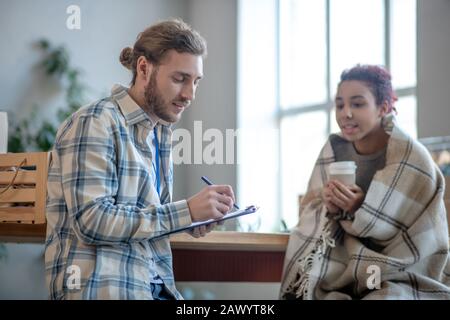 Junger Mann steht schriftlich, Mädchen sitzt trinkend Kaffee. Stockfoto