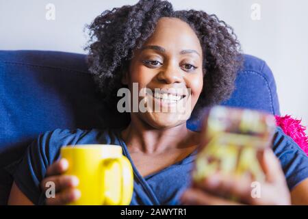 Nahaufnahme einer glücklichen Frau, die Tee trinkt und mit dem Smartphone telefoniert Stockfoto