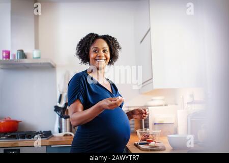 Portrait fröhliche schwangere Frau, die in der Küche isst Stockfoto