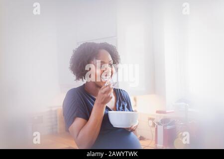 Fröhliche schwangere Frau, die in der Küche isst Stockfoto