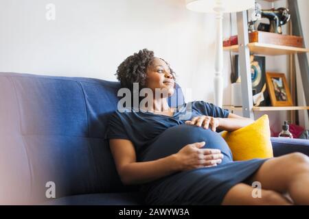 Ruhige schwangere Frau, die sich auf dem Sofa entspannen kann Stockfoto