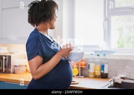 Schwangere Frau isst und schaut auf das Küchenfenster Stockfoto