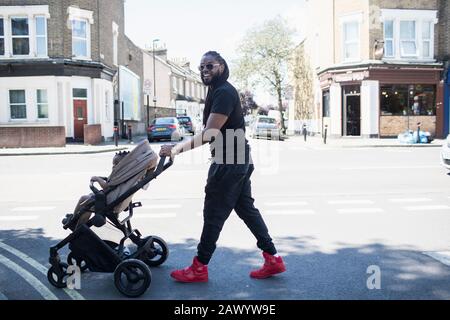 Portrait glücklicher Vater treibt kleinen Sohn in Kinderwagen auf der sonnigen städtischen Straße Stockfoto