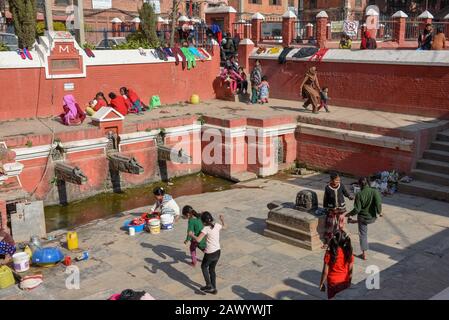 Patan, Nepal - 24. Januar 2020: Frauen waschen Kleidung und Töchter, die am Brunnen von Patan in der Nähe von Kathmandu auf Nepal spielen Stockfoto