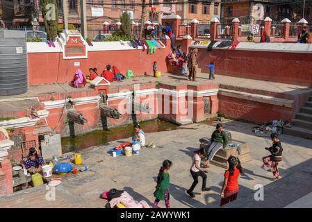 Patan, Nepal - 24. Januar 2020: Frauen waschen Kleidung und Töchter, die am Brunnen von Patan in der Nähe von Kathmandu auf Nepal spielen Stockfoto