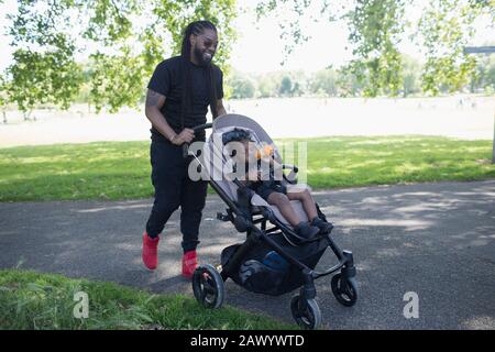 Vater schiebt Kleinkindsohn in Kinderwagen im Park Stockfoto