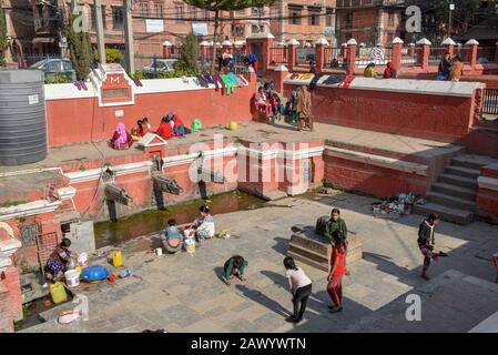 Patan, Nepal - 24. Januar 2020: Frauen waschen Kleidung und Töchter, die am Brunnen von Patan in der Nähe von Kathmandu auf Nepal spielen Stockfoto