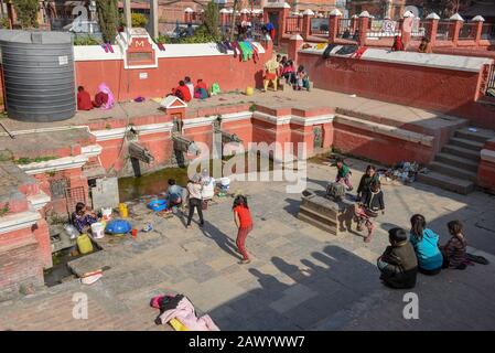 Patan, Nepal - 24. Januar 2020: Frauen waschen Kleidung und Töchter, die am Brunnen von Patan in der Nähe von Kathmandu auf Nepal spielen Stockfoto