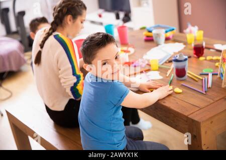 Portrait niedlicher Junge mit Daung-Syndrom-Farbgebung am Tisch mit Schwester Stockfoto