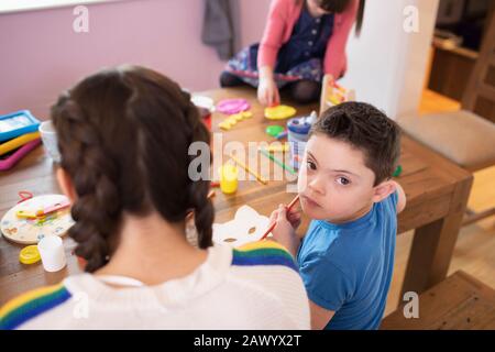 Portrait niedlicher Junge mit Daung-Syndrom-Farbgebung am Tisch mit Geschwistern Stockfoto